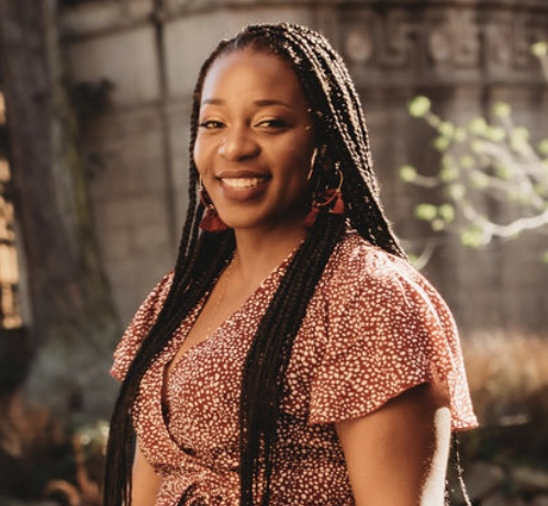 African-American woman with long braids pictured outdoors at the palace of fine arts wearing polka dot red wine dress with bright smile on a nice sunny day in San Francisco
