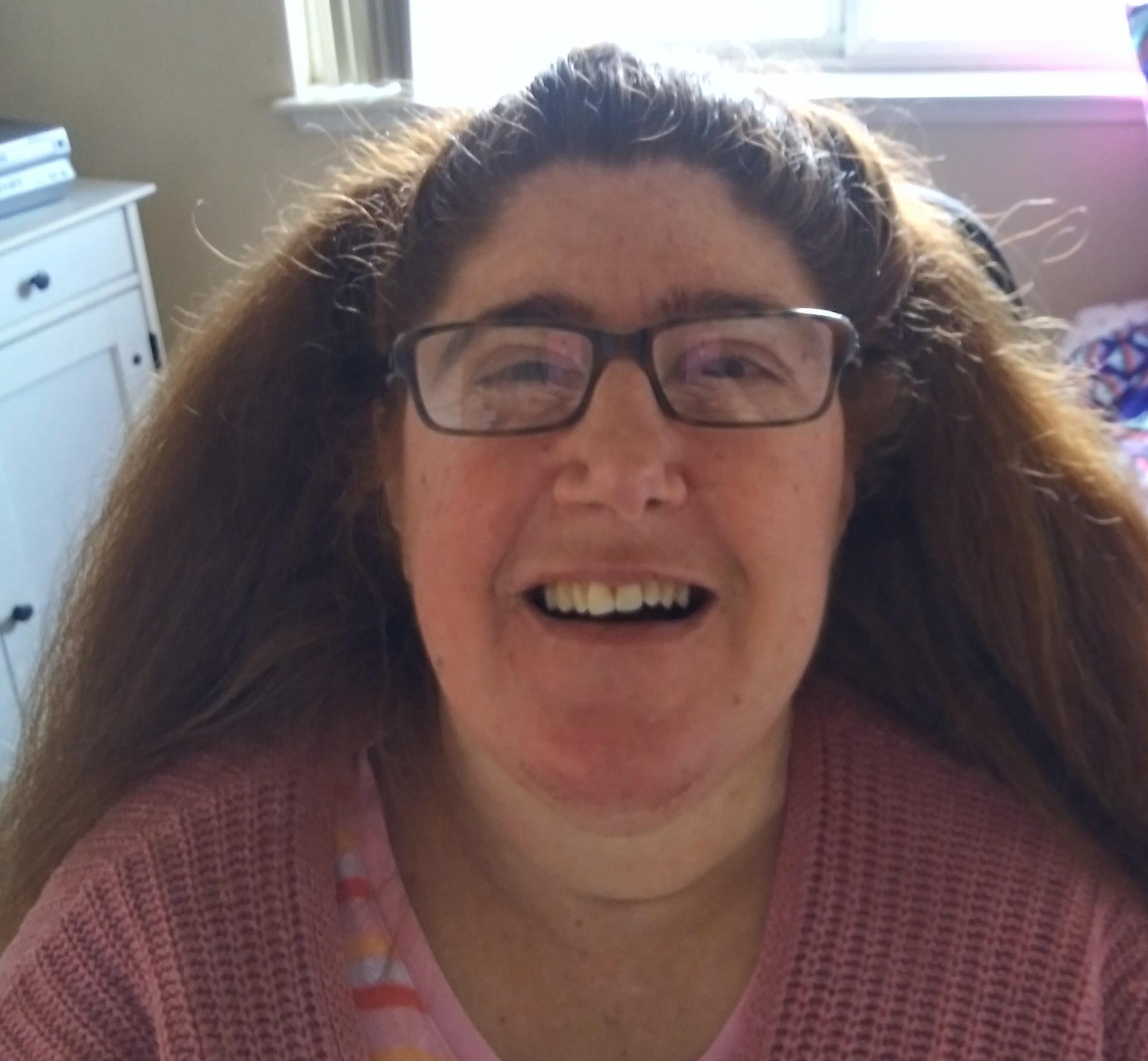 Jennifer is a Caucasian woman with glasses and auburn shoulder-length hair, wearing a pink knit sweater.